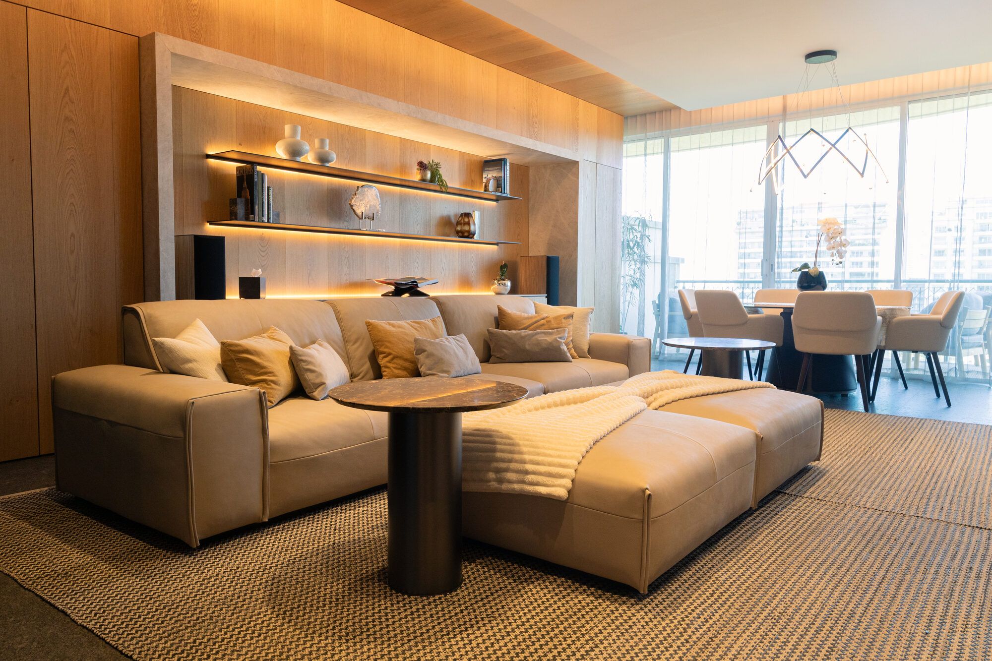 Sala de estar con sofá modular, estantería iluminada y comedor al fondo