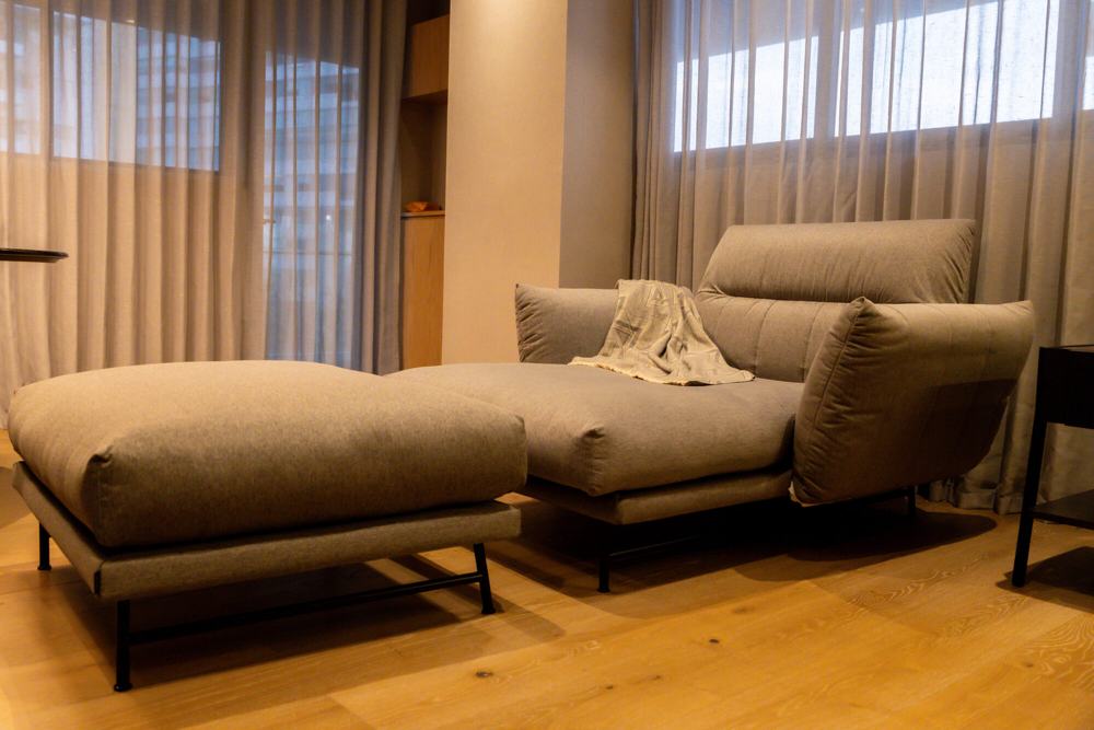 Chaise longue y otomana tapizadas junto a cortinas