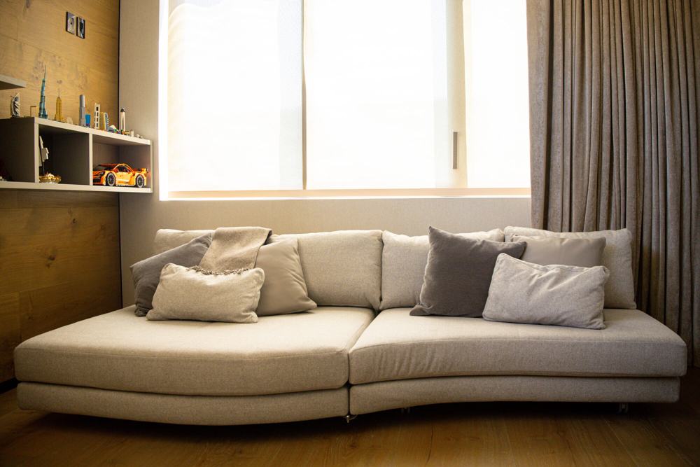 Sofá curvo bajo una ventana con cortinas